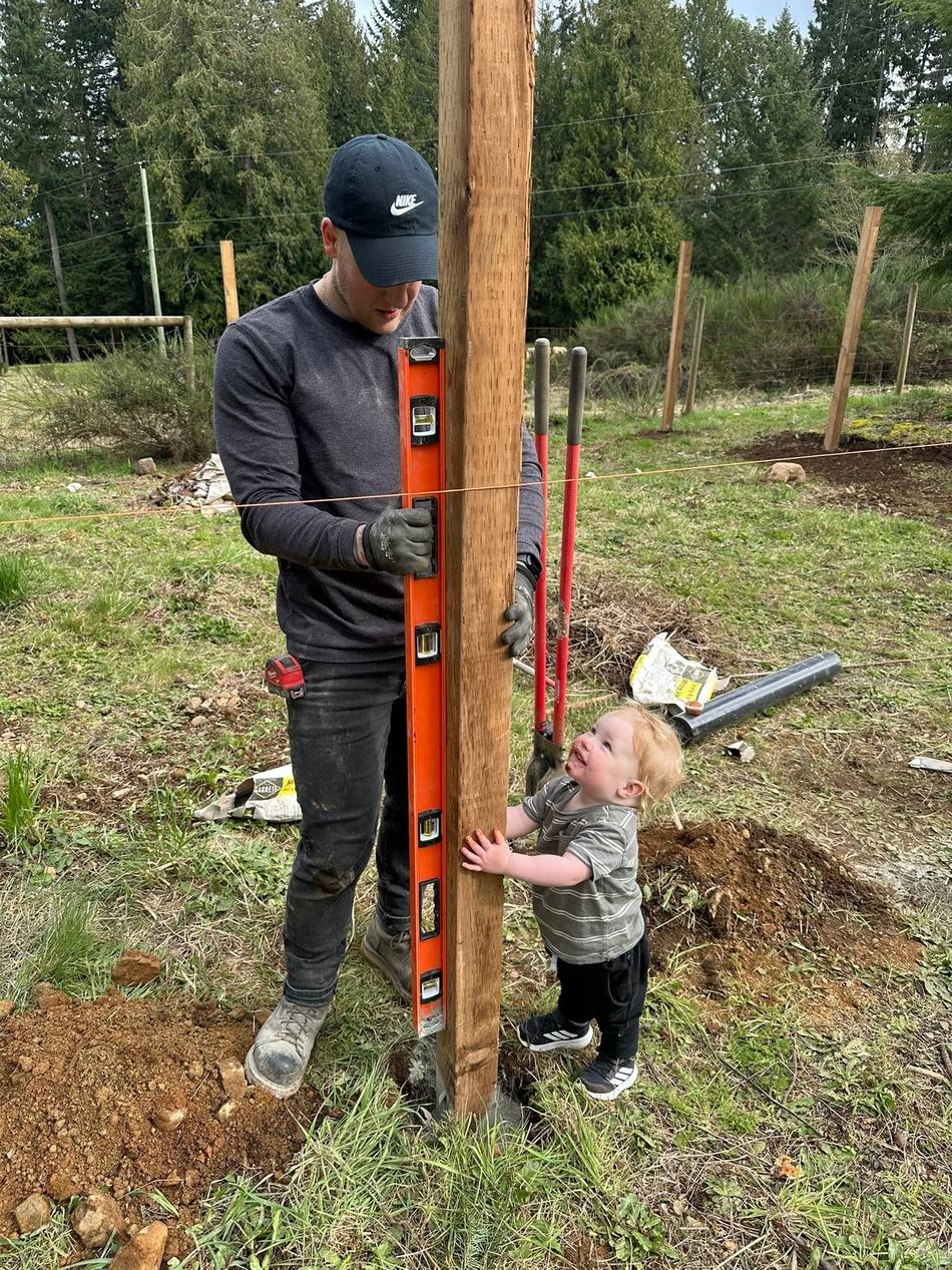 Valley Reign Contracting setting a fence post plumb with a level while a small child helps