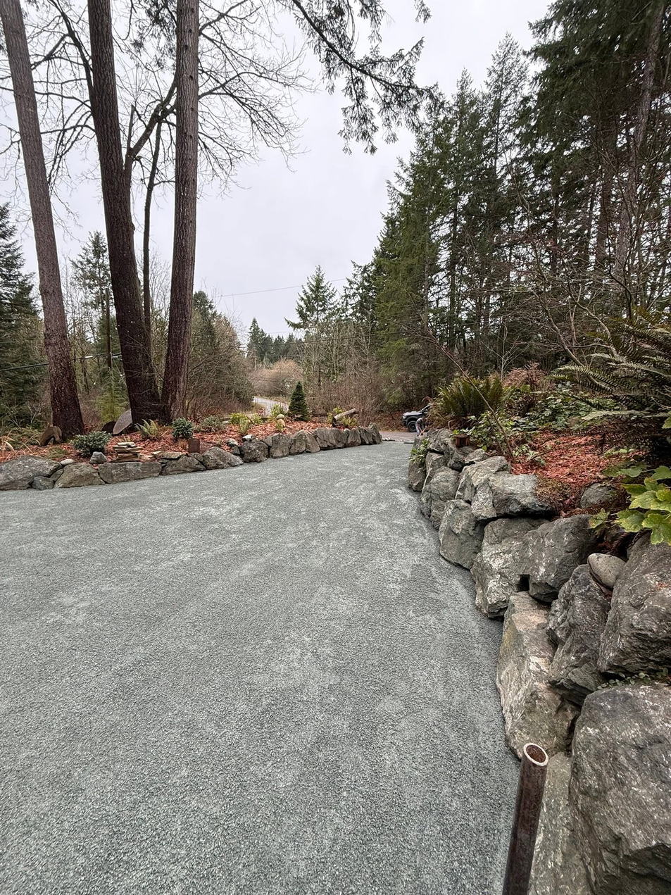 Finished driveway running between a rock retaining wall and mature timber