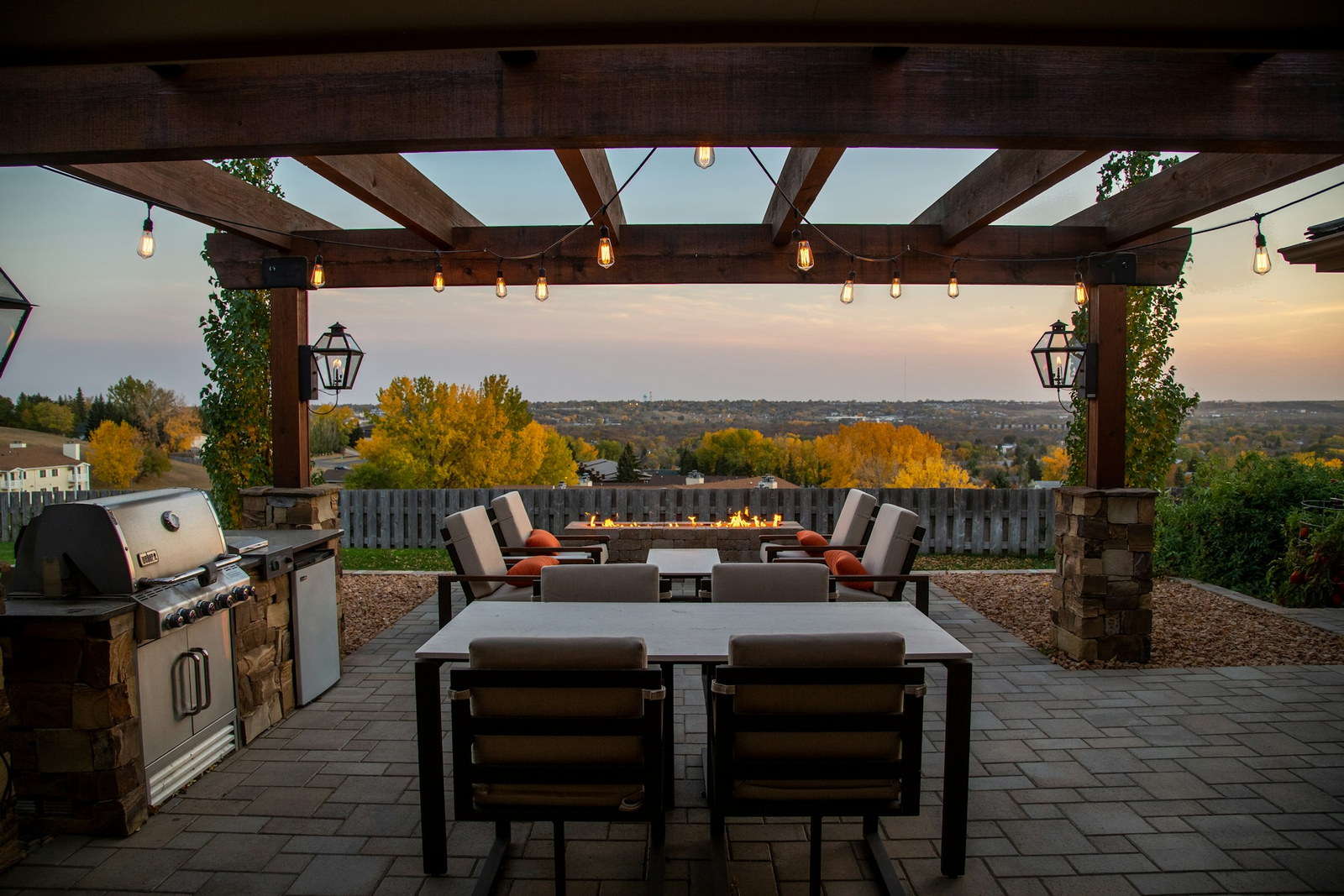 Covered outdoor kitchen and stone patio lit at dusk