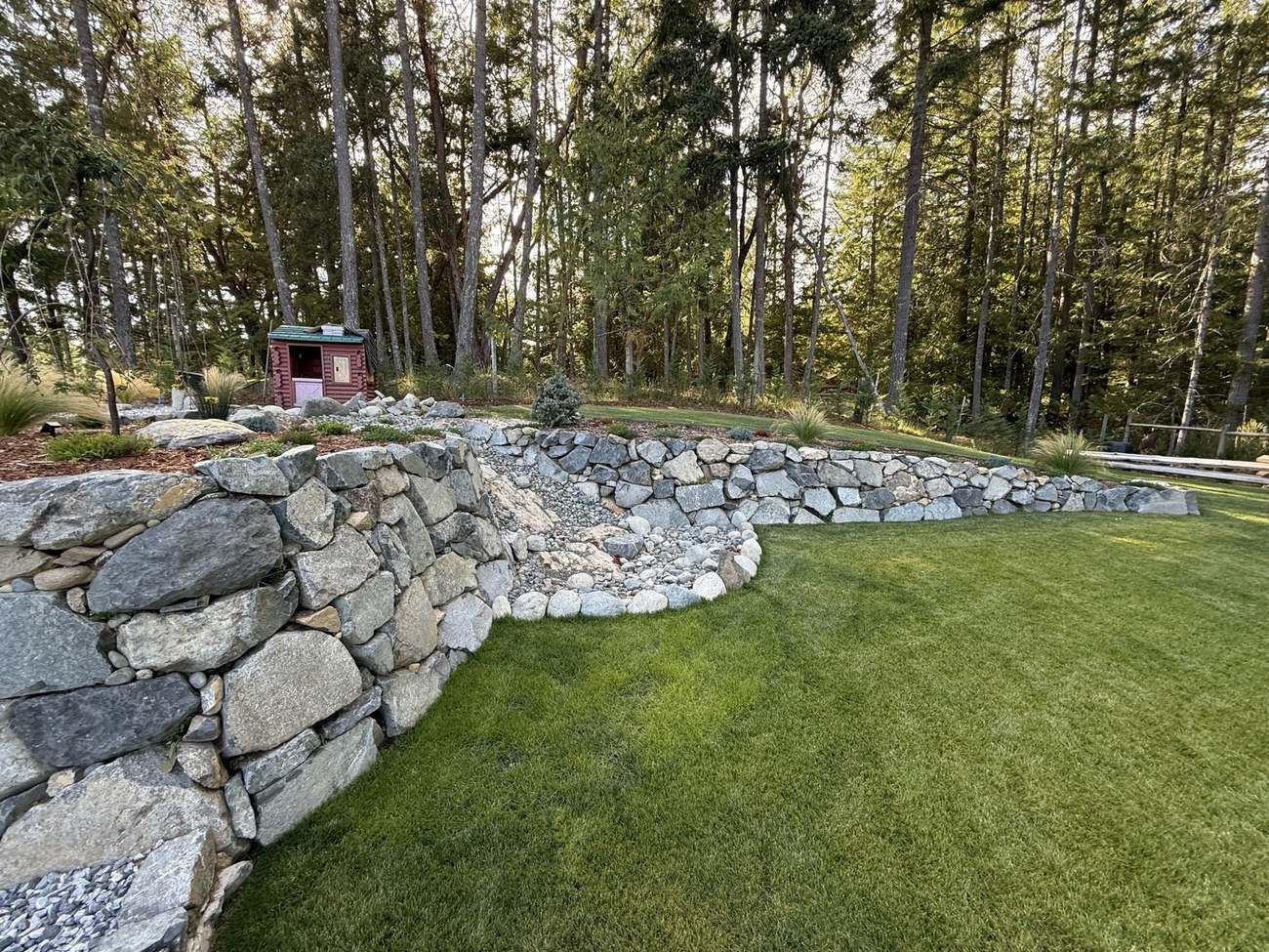 Curved armour stone retaining wall with a dry creek bed running through a lawn